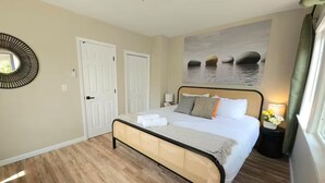 A bedroom with a bed, two doors, a mirror, a painting, and a nightstand with flowers. - Bright Bungalow steps from Caltech & PCC, Close to the Rose Bowl, Kingsize Bed! (Pasadena)