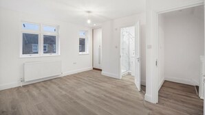 Una habitación amplia con suelo de madera, paredes blancas y un ventanal grande.