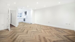 Una habitación amplia con piso de madera en diseño espiga, paredes blancas y luces empotradas en el techo.