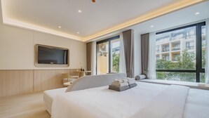 A modern hotel room with a large bed, a flat-screen TV mounted on the wall, a small table with a pineapple, and a view of the city through large windows. - Sea Heaven Elegant Studio, Forrest View 2229 (Sakhu -  Thalang)
