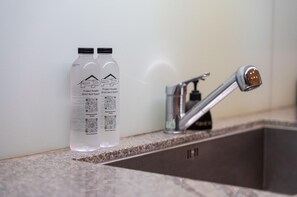 Twee flessen met etiketten en QR-codes op een granieten aanrecht, naast een moderne kraan.
