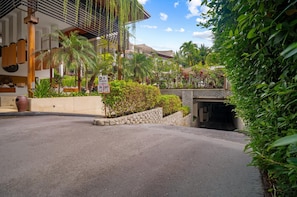 L’entrée d’un hôtel, avec un panneau indiquant un parking, une végétation luxuriante et un mur en pierre.