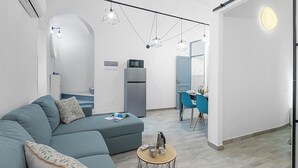 A modern living room with a sectional sofa, a small round coffee table, and a dining area with a blue chair and table. - Saro House, Centre Apartment for 6, Sanremo, Italy (Sanremo)
