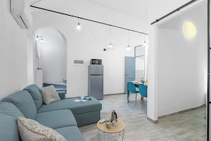 En moderne stue med en hjørnesofa, et spiseområde med blå stole og et køkken med et køleskab.
