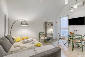 Un soggiorno moderno e luminoso con un divano, un tavolo da pranzo e una TV a parete.