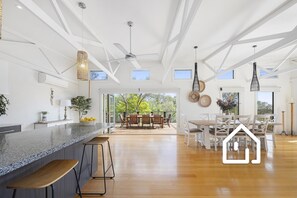 A spacious kitchen with a large island, wooden flooring, and a dining area with a view of the outdoors. - Nautilus Rise *1 NIGHT FREE* Panoramic Bay & Coastal Views (Rye)