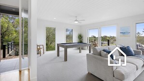 Ein geräumiges Wohnzimmer mit Billardtisch, einer Couch und großen Fenstern mit Blick ins Freie.