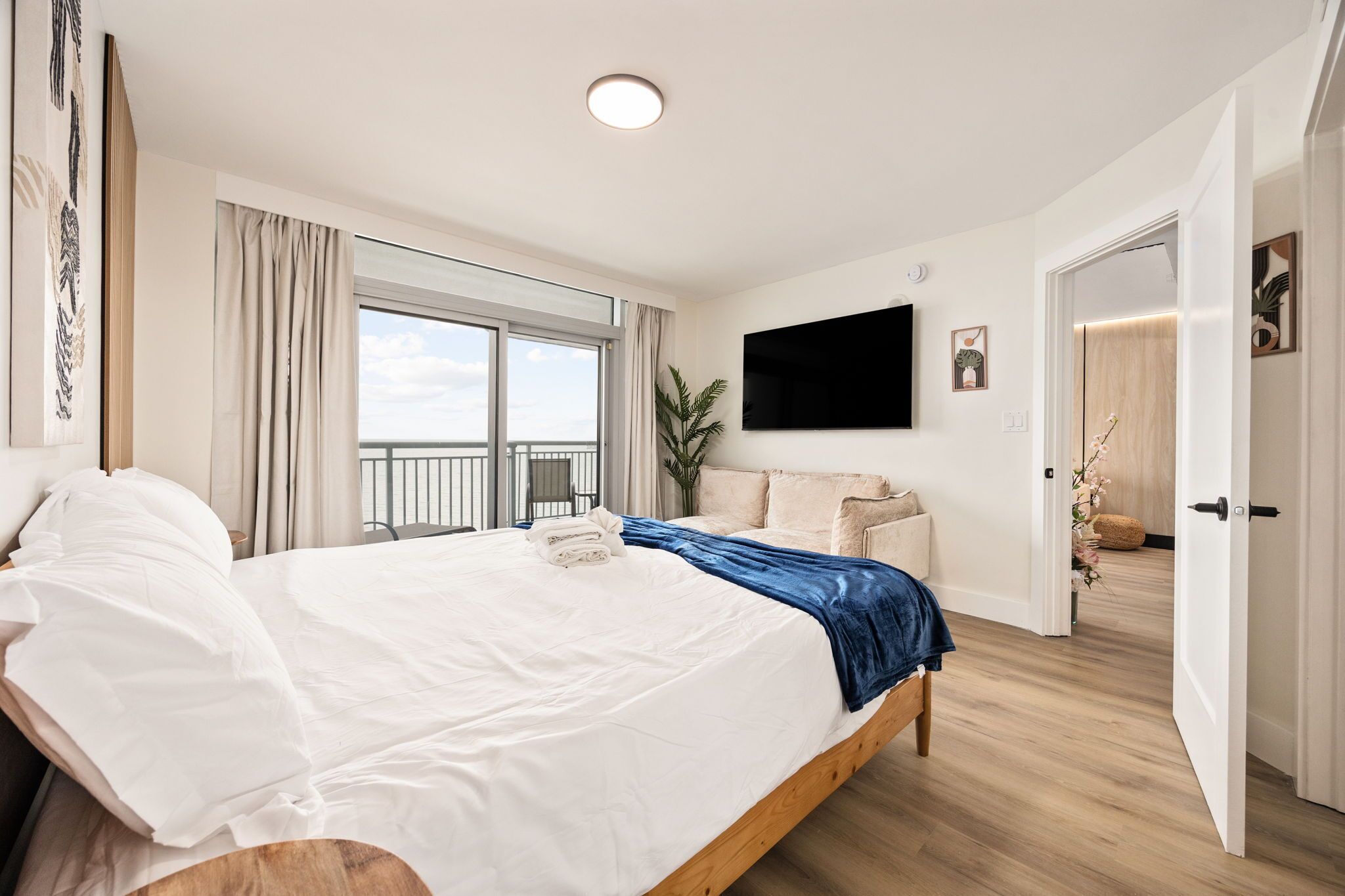 Une chambre d’hôtel moderne dotée d’un grand lit, d’une télévision à écran plat, d’un balcon avec vue et d’un plancher en bois.