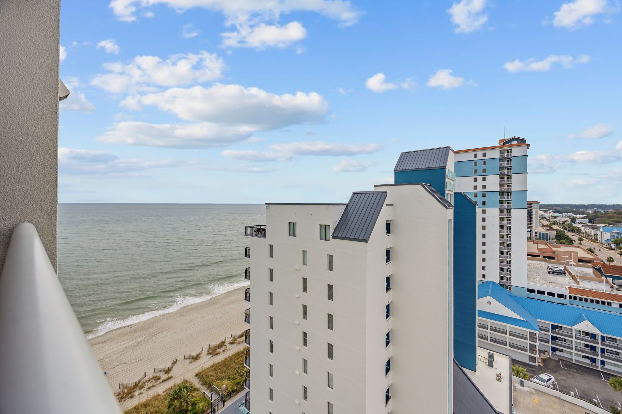 A high-rise hotel with multiple floors, a beach view, and a parking area visible in the background.