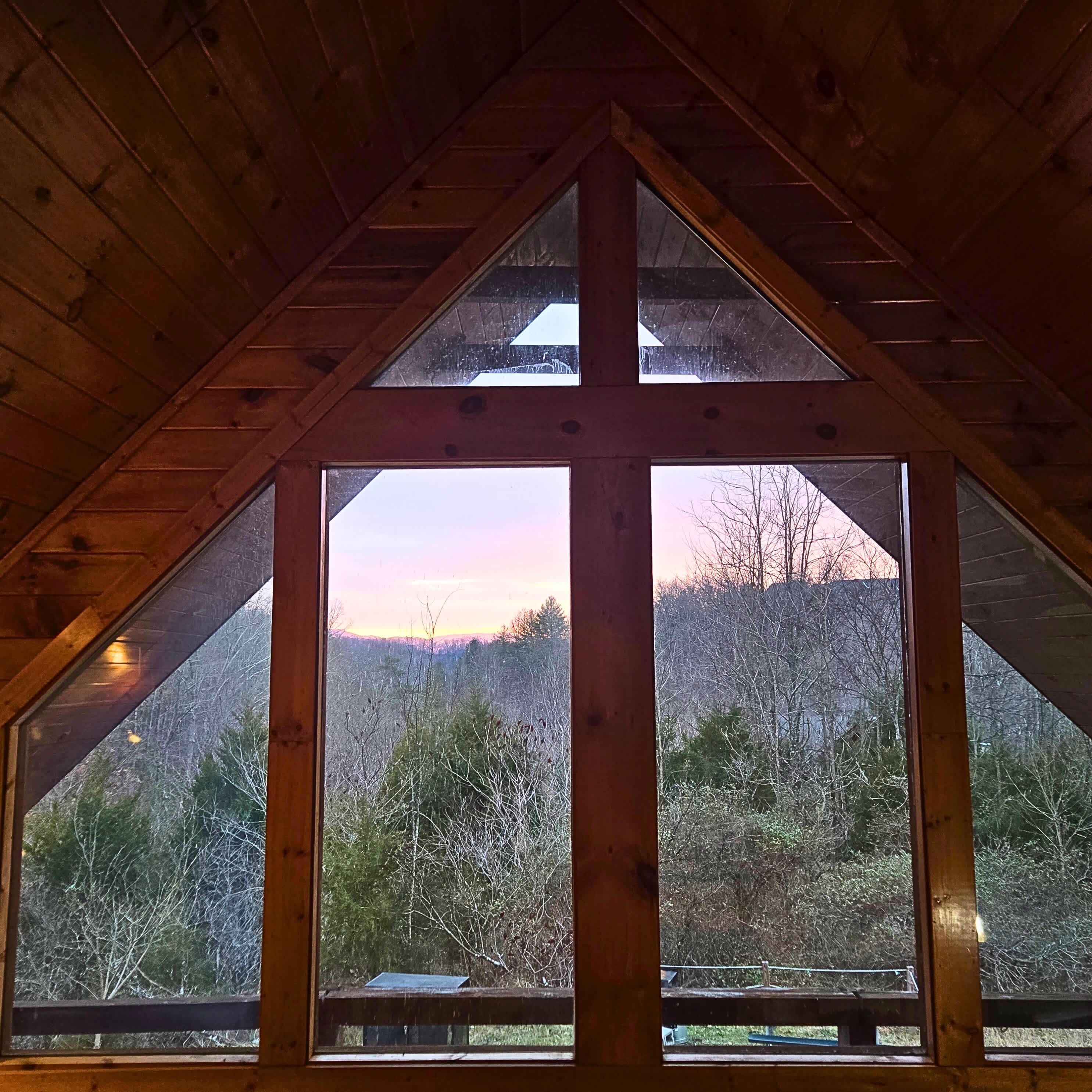 Une fenêtre triangulaire donnant sur un paysage boisé.