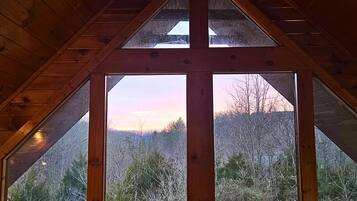 Une fenêtre triangulaire donnant sur un paysage boisé.