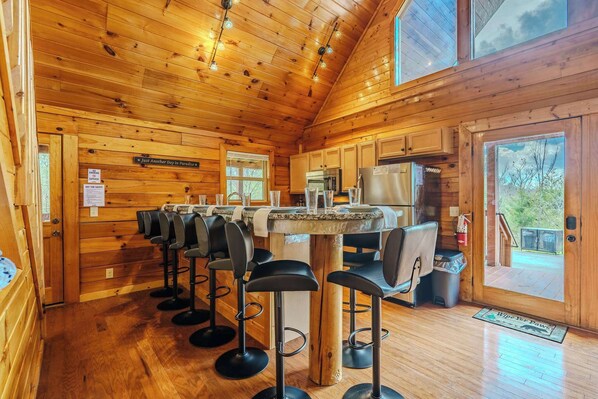 A wooden cabin interior with a kitchen area, bar stools, and a large window. - Private Hot Tub • Game Loft • Pet Friendly (Sevierville)