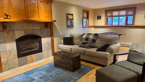 A living room with a stone fireplace, a sofa, a coffee table, and a window with blinds. - Habart Retreat - Country Living at its Best (Golden)