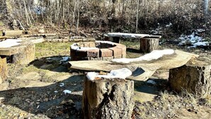 A rustic outdoor setting with wooden benches and a fire pit, surrounded by trees and a snowy ground. - Habart Retreat - Country Living at its Best (Golden)