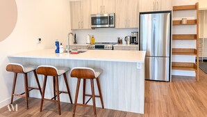 Une cuisine moderne dotée d’un îlot central, de tabourets de bar, d’appareils électroménagers en acier inoxydable et de meubles de rangement en bois.