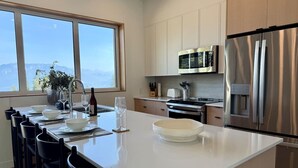 Een moderne keuken met een groot eiland, roestvrijstalen apparatuur en uitzicht op bergen vanuit het raam.