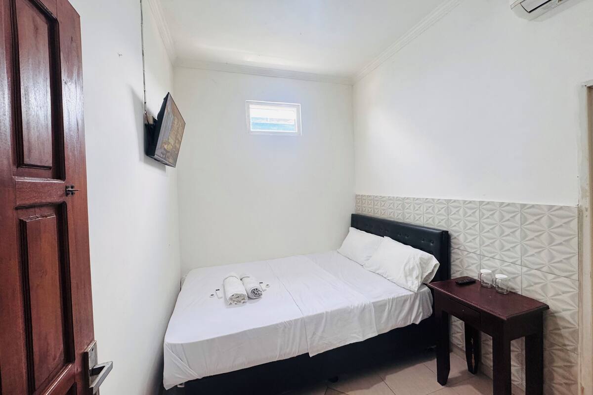 Una habitación pequeña y limpia con una cama individual, una mesita y una ventana.