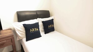 Ein Hotelzimmer mit einem Bett, zwei Kissen mit dem Schriftzug 'ARBA HOSPITALITY' und einem Nachttisch aus Holz. Eine schlichte weiße Wand ist ebenfalls zu sehen.