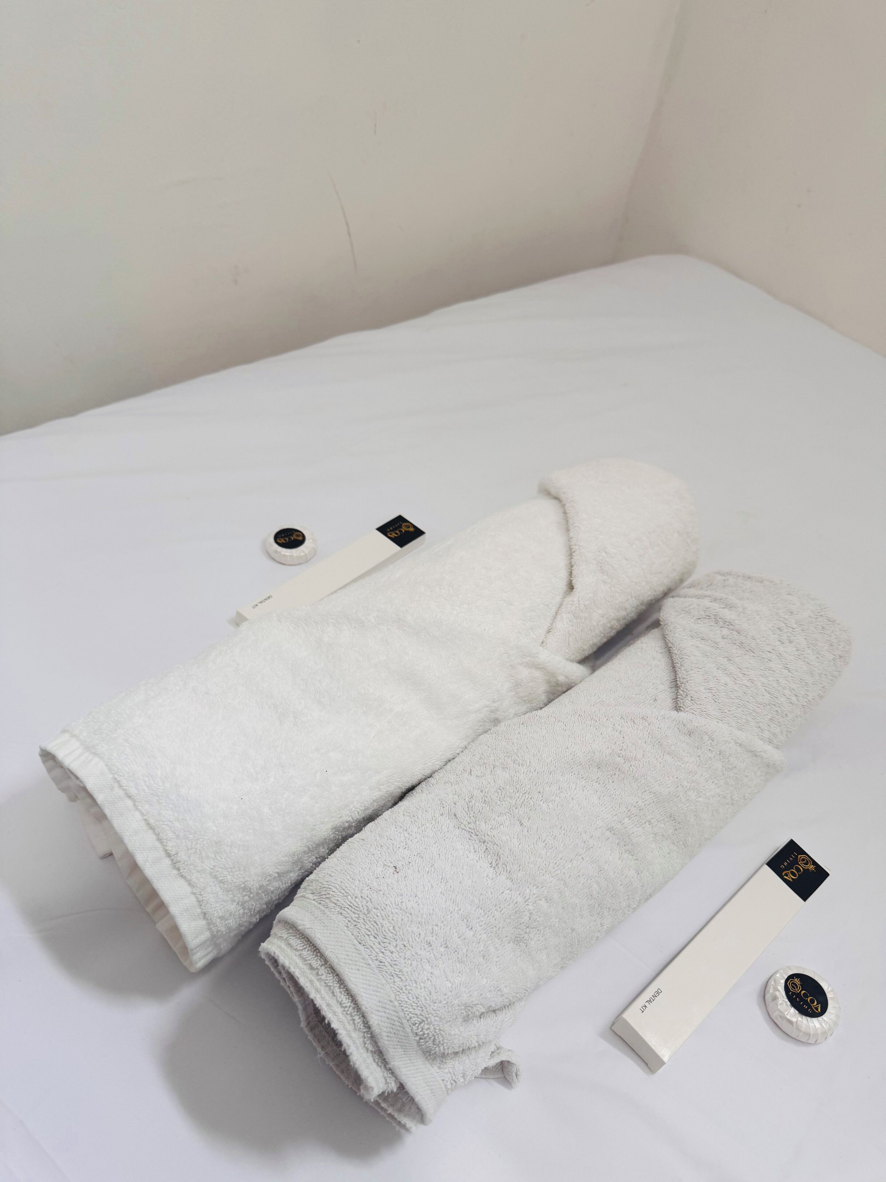 A neatly folded white towel and a white bottle with a black label on a white surface.