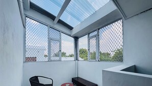 Ein kleiner, abgeschlossener Balkon mit Stadtblick, ausgestattet mit einer Holzbank, einem kleinen runden Tisch und einem schwarzen Stuhl.