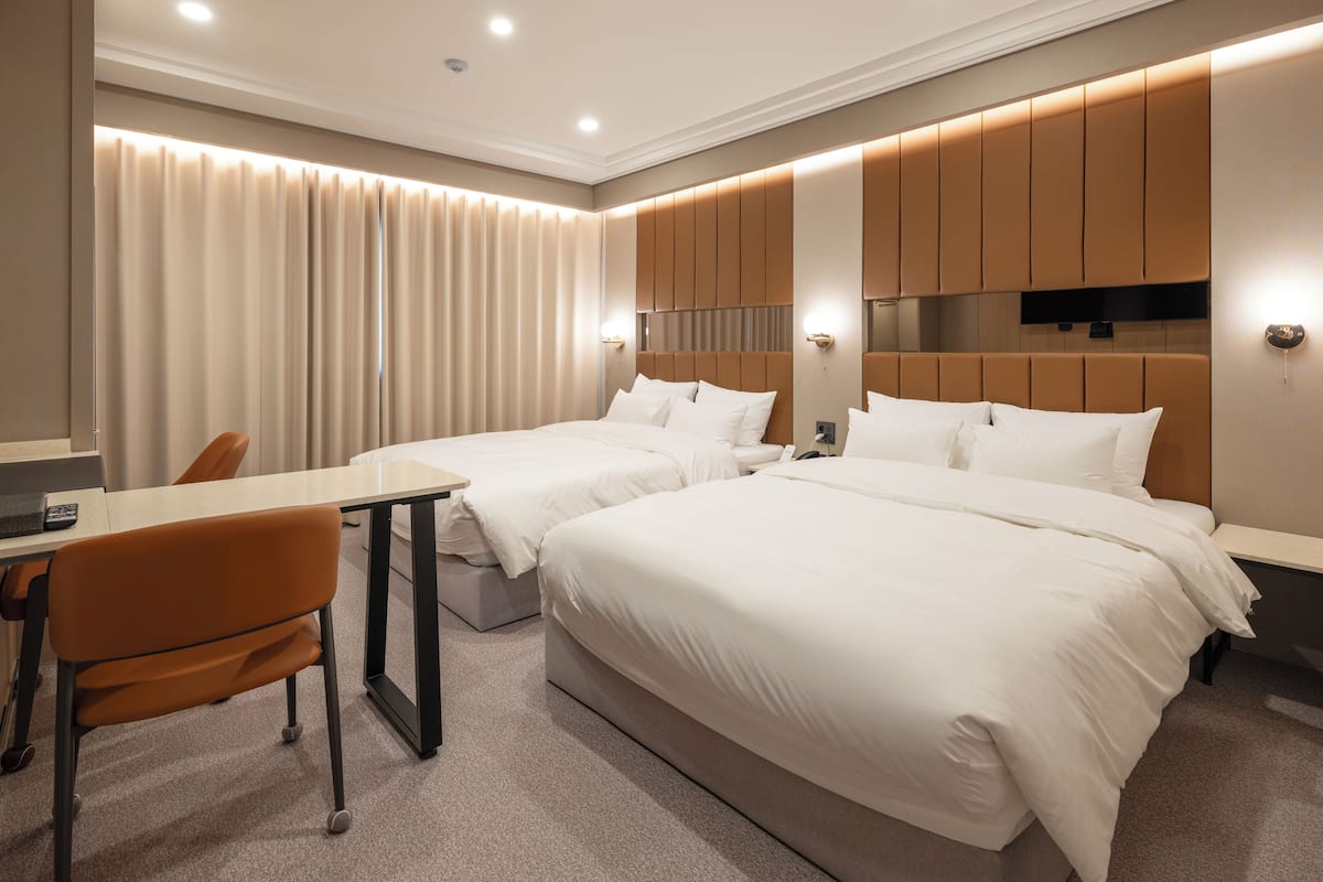 A hotel room with two beds, a desk, and a chair.