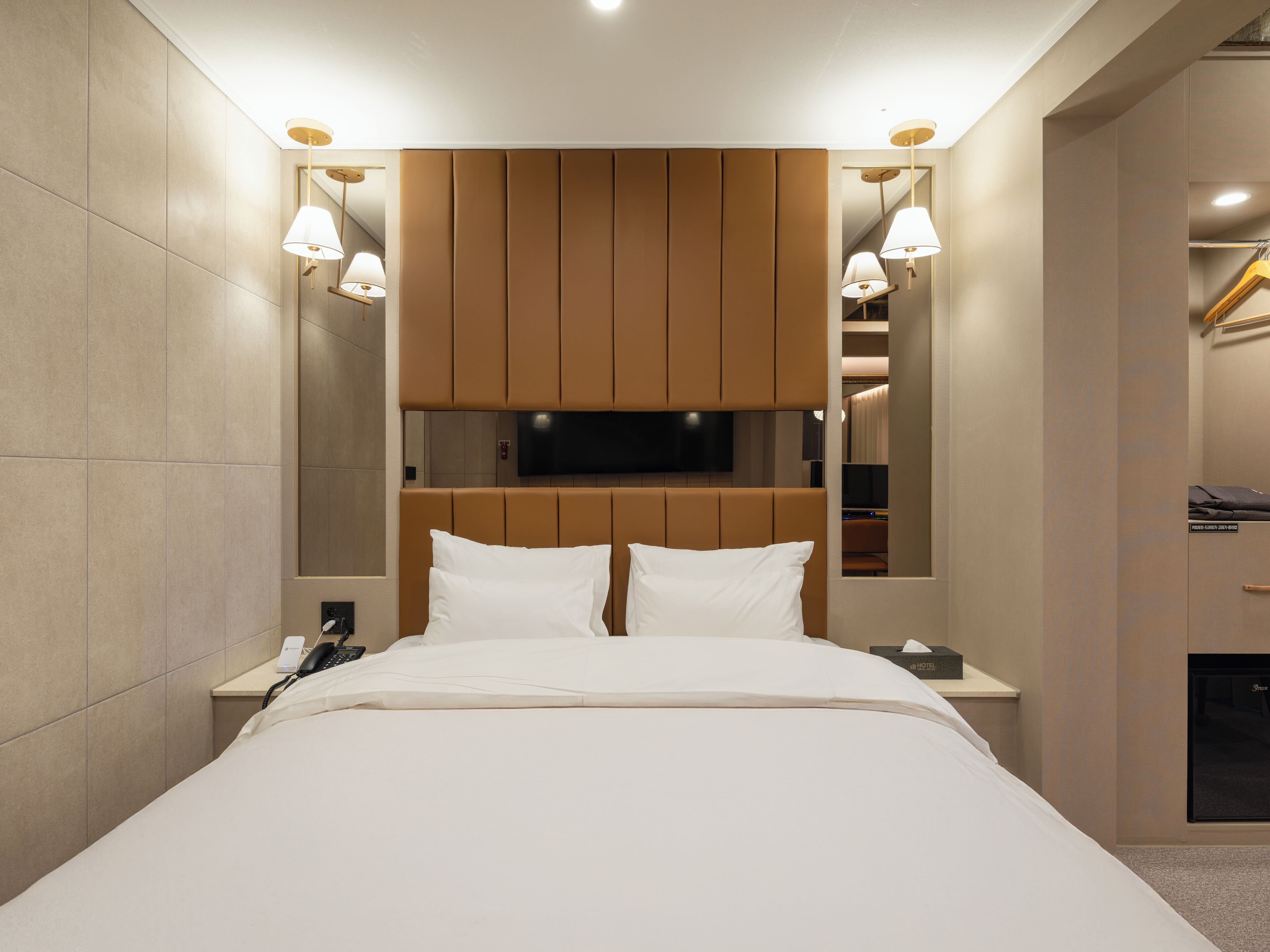 Una habitación de hotel moderna con una cama grande, un televisor de pantalla plana montado sobre ella, lámparas de noche y un armario empotrado con espejo.