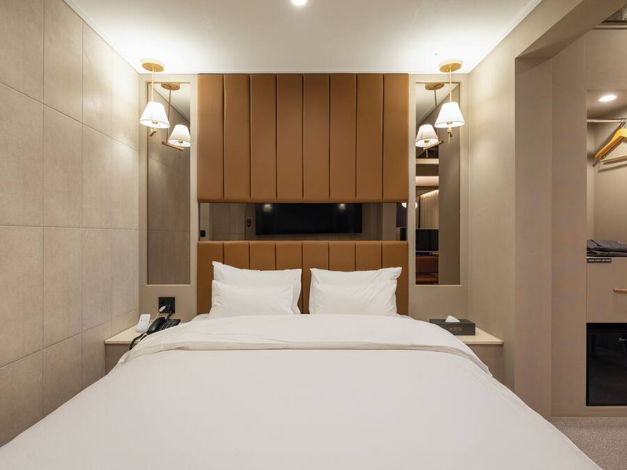 Una habitación de hotel moderna con una cama grande, un televisor de pantalla plana montado sobre ella, lámparas de noche y un armario empotrado con espejo.