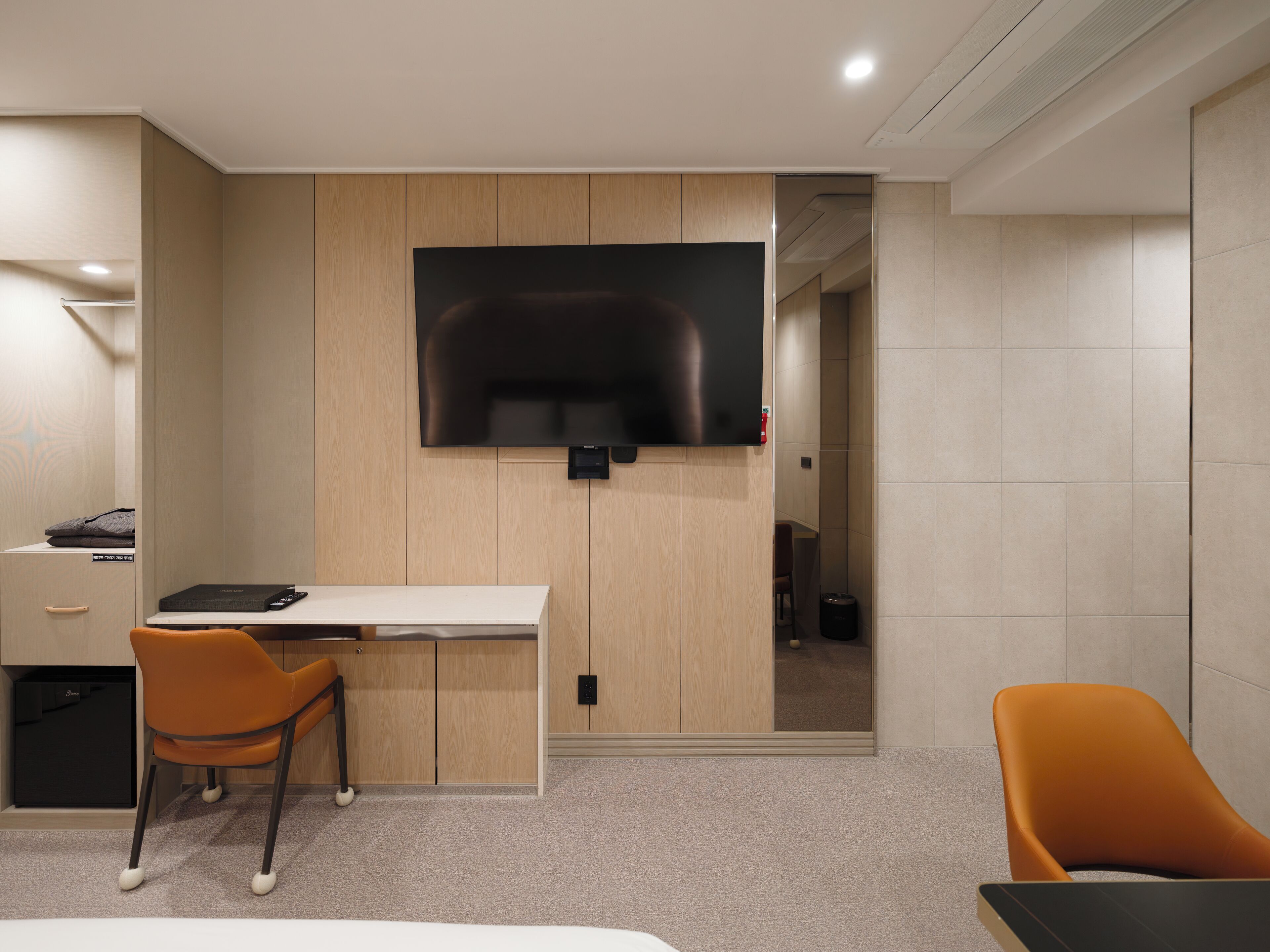 A modern hotel room with a flat-screen TV mounted on the wall, a desk with a chair, and a bed.