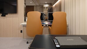 Una camera d'albergo con una scrivania, due sedie, una televisione e un minibar.