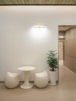 Un interior moderno con una mesa redonda y dos taburetes, una planta en maceta y una lámpara de pared.