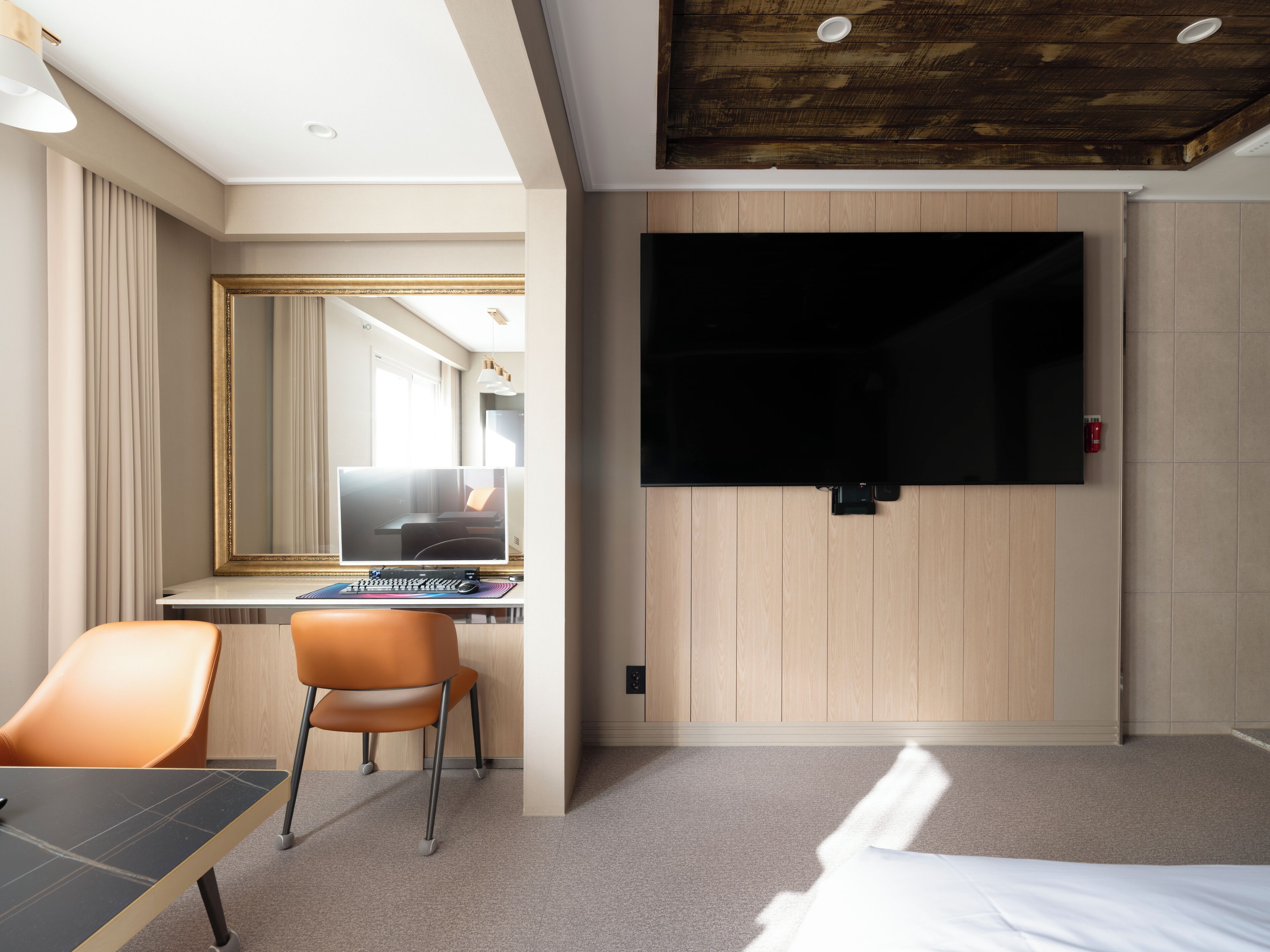 A hotel room with a desk, chair, bed, and a large flat-screen TV mounted on the wall.