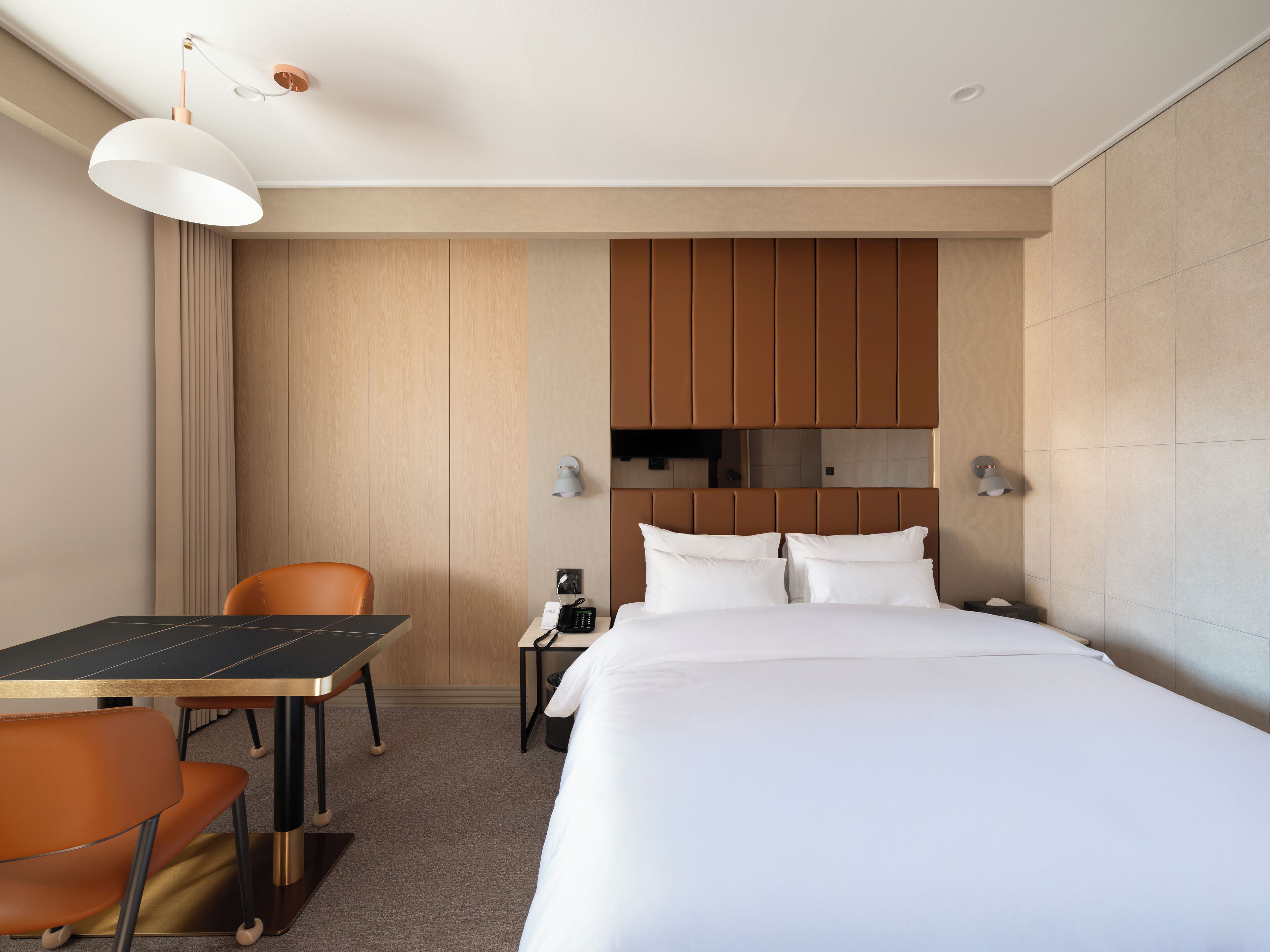 Habitación de hotel con cama, escritorio, silla, teléfono y lámpara de pared.