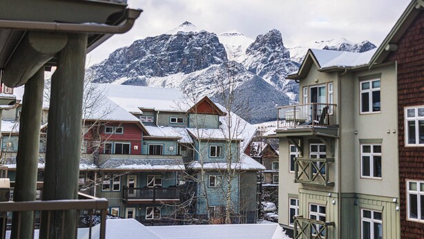 Una fila di edifici a più piani con tetti imbiancati dalla neve e montagne sullo sfondo.