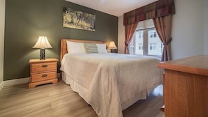 Una camera da letto con un letto di legno, due comodini con lampade, una ventola a soffitto, una finestra con tende e un quadro appeso al muro.