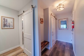 A hallway with a wooden floor, white walls, and a framed picture. There are two doors, one with a sliding mechanism and another with a traditional door. A small wooden shelf is visible on the floor. - Axtel 310 Beautiful 1-bedroom condo in Mt Crested Butte perfect for your getaway (Crested Butte)
