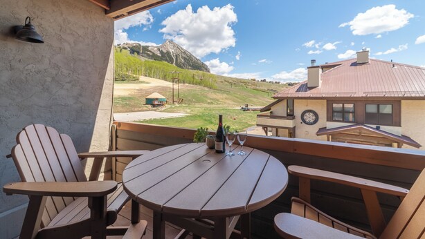 Un terrazzo in legno con un tavolo rotondo e poltrone Adirondack, con vista su un paesaggio montuoso.