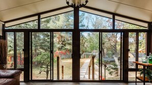 Un'ampia stanza con grandi porte scorrevoli in vetro che si aprono su un giardino sul retro, con un pontile in legno, uno stagno e alberi.