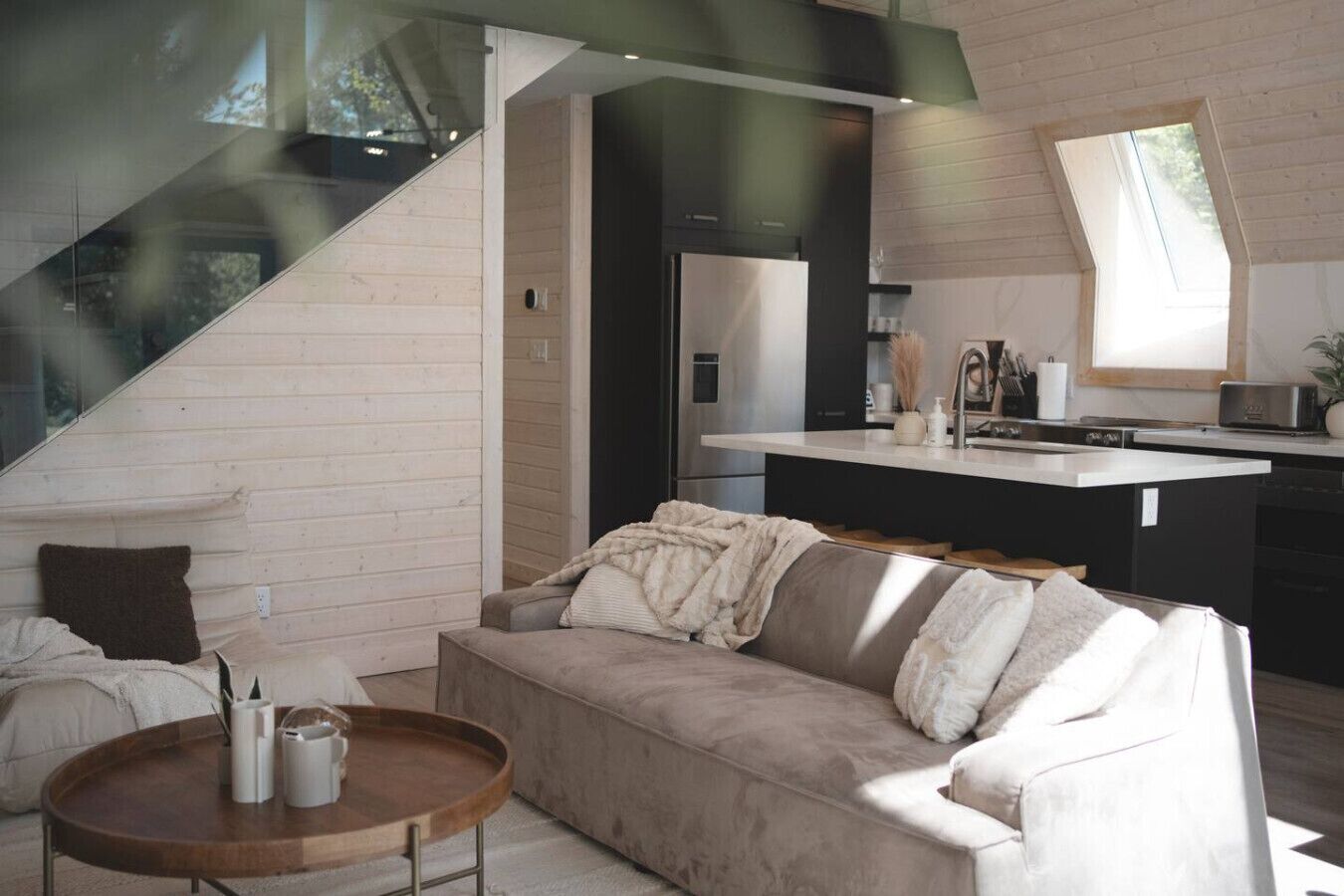 Una sala de estar moderna con un sofá, una mesa redonda de madera y una cocina con encimera y electrodomésticos.