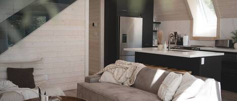 Una sala de estar moderna con un sofá, una mesa redonda de madera y una cocina con encimera y electrodomésticos.
