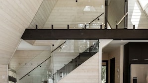 Una sala de estar moderna con techo de madera, una escalera, un sofá, una mesa de centro y una zona de cocina.