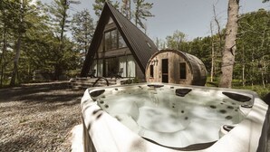 Una cabaña con jacuzzi, un barril de madera y un techo triangular.