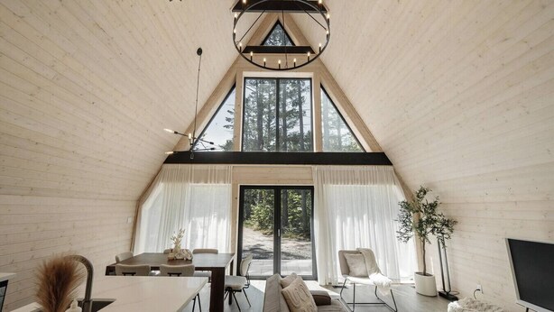 Un interior acogedor con techos altos, una zona de comedor, sofá y grandes ventanales con vistas al bosque.