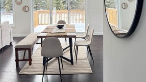 Un comedor moderno con una mesa grande, sillas y un banco. Se observan amplias ventanas con vistas a una terraza de madera.