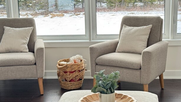 Una habitación con dos sillones grises, una cesta tejida y una planta en maceta sobre una bandeja de madera redonda.