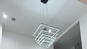Una habitación amplia con techo alto, una lámpara moderna de diseño geométrico, estanterías empotradas y un gran ventanal.