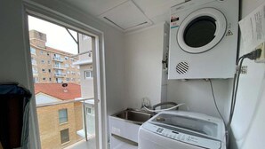 Una lavandería con lavadora y secadora, una ventana y vista a un edificio exterior.