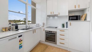 Una cocina moderna con armarios blancos, horno de acero inoxidable, microondas y un amplio ventanal con vistas al exterior.