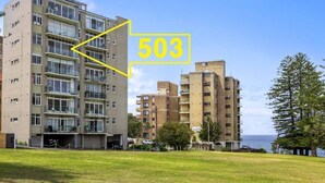 Un edificio residencial de varios pisos con balcones, un área verde en la parte delantera y una vista despejada del mar.