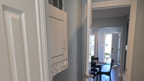 A laundry room with a washer and dryer, a small heater, and a door leading to a dining area with a table and chairs. - Family & Pet Friendly 1-BD Apt mins from Downtown, UH, Med Center & Attractions (Houston)