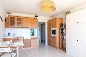 A modern kitchen with wooden cabinets, a white countertop, and a dining area with a table and chairs. - L'appartement Cala Nova (BORMES LES MIMOSAS)